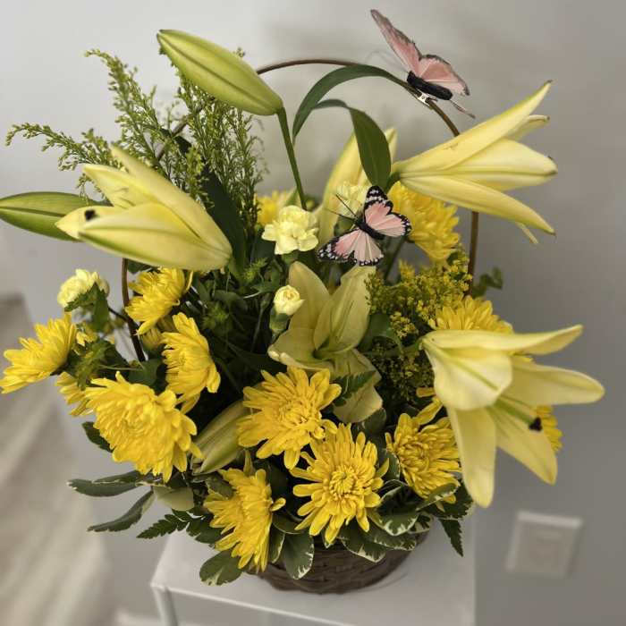 Basket arrangement of yellow lilies and chrysanthemums with pink decorative butterflies.