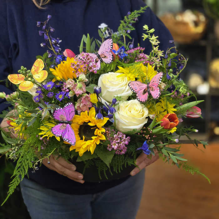 Colorful mixed flower arrangement in a black container with butterfly picks