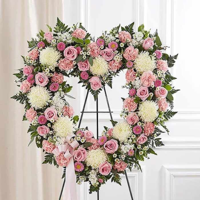Heart-shaped floral wreath with pink roses and white blooms on a stand