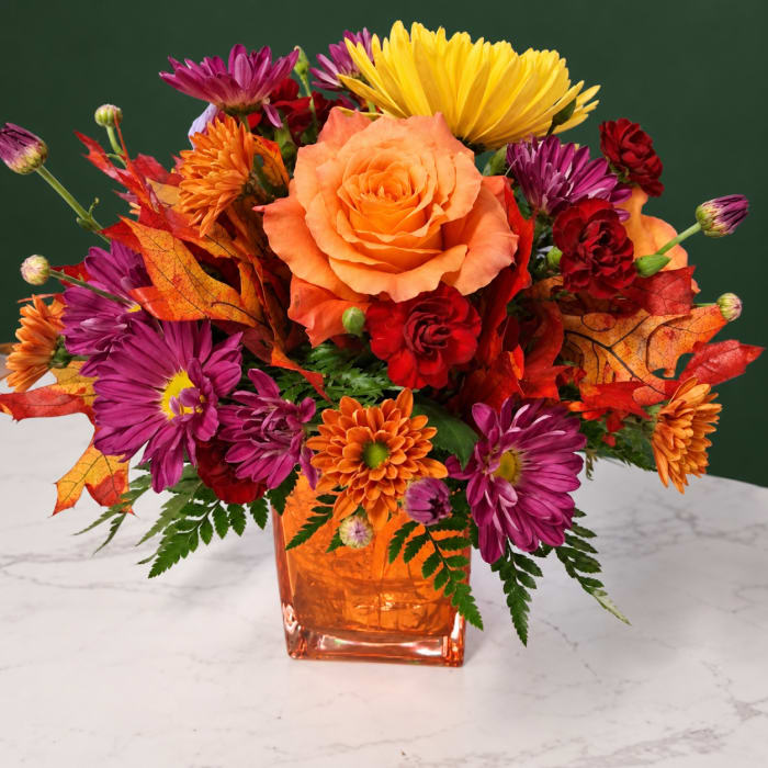 Orange roses and purple chrysanthemums in an orange glass vase