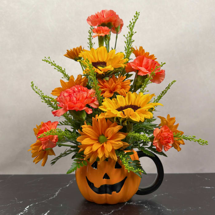 Orange and yellow flower arrangement in a jack-o'-lantern mug