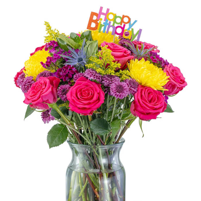 Bright mixed bouquet of pink roses and yellow chrysanthemums in a glass vase with a birthday sign