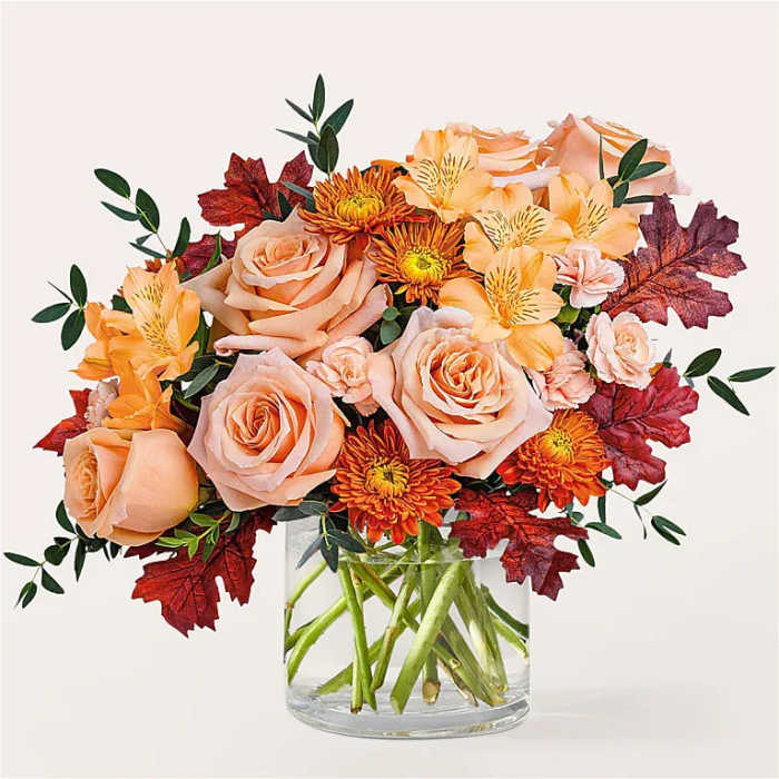 Peach roses and orange flowers in a clear glass vase