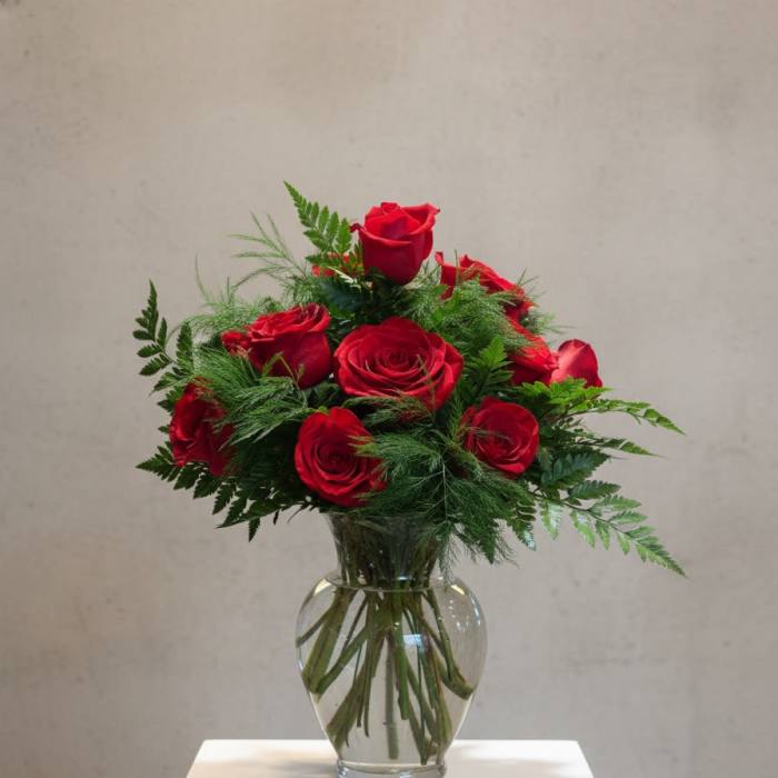 Red roses arranged in a clear glass vase with greenery