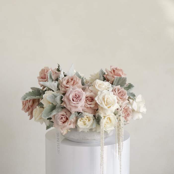 Blush and white roses arranged in a low round box.