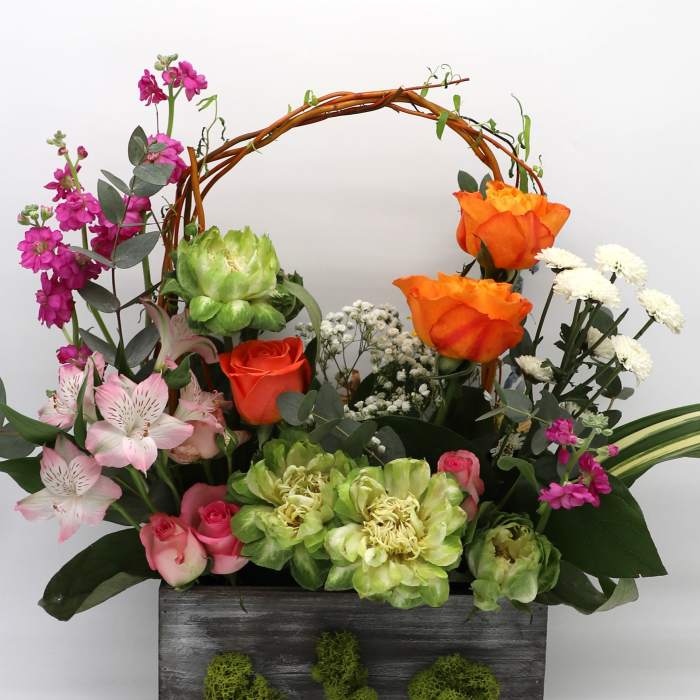 Mixed floral arrangement in a dark wooden box with an arched twig handle