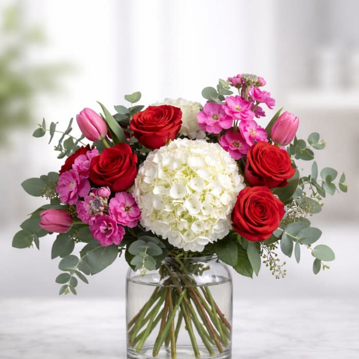 Bouquet of red roses, pink tulips, and white hydrangea in a glass vase