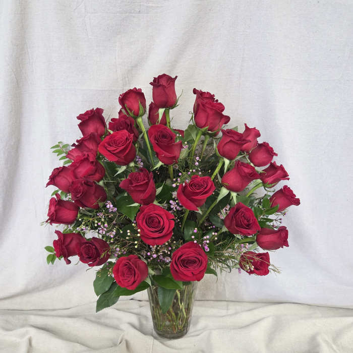 Tall clear vase filled with numerous red roses and small pink filler flowers