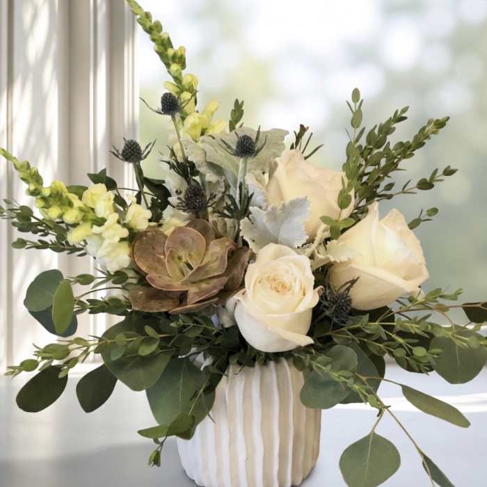 White roses and snapdragons in a ribbed vase with eucalyptus and succulents