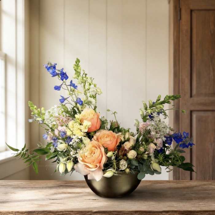 Peach roses and blue flowers arranged in a dark bowl vase
