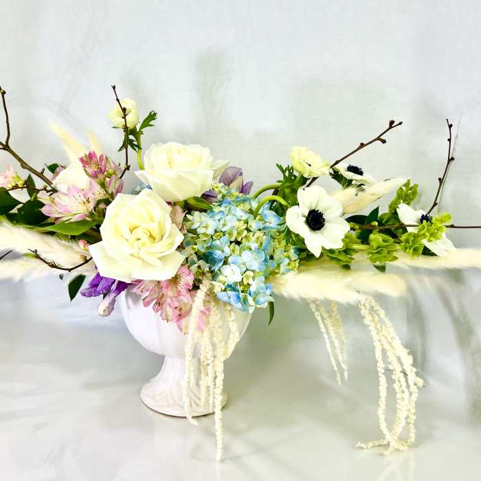 White roses and blue hydrangeas in a white vase with branches and feathers