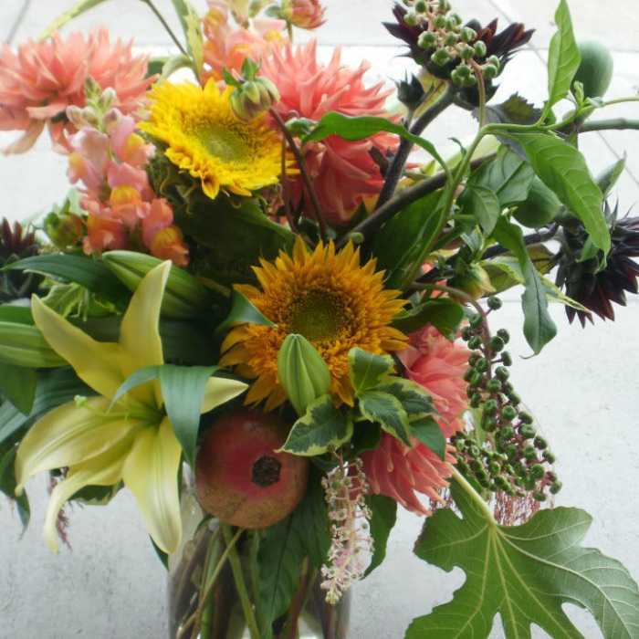 Loose garden-style bouquet with yellow sunflowers, peach dahlias, and lilies in a clear glass vase