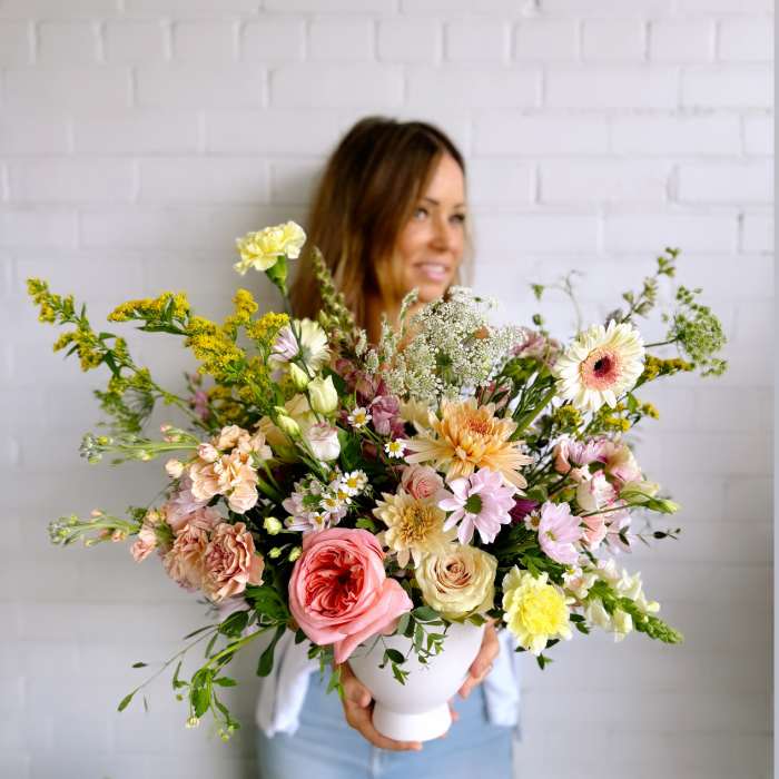 Large pastel bouquet in a white vase held by a woman
