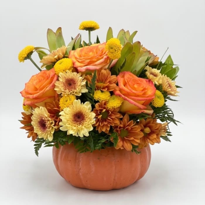 Orange roses and yellow daisies arranged in a pumpkin-shaped container
