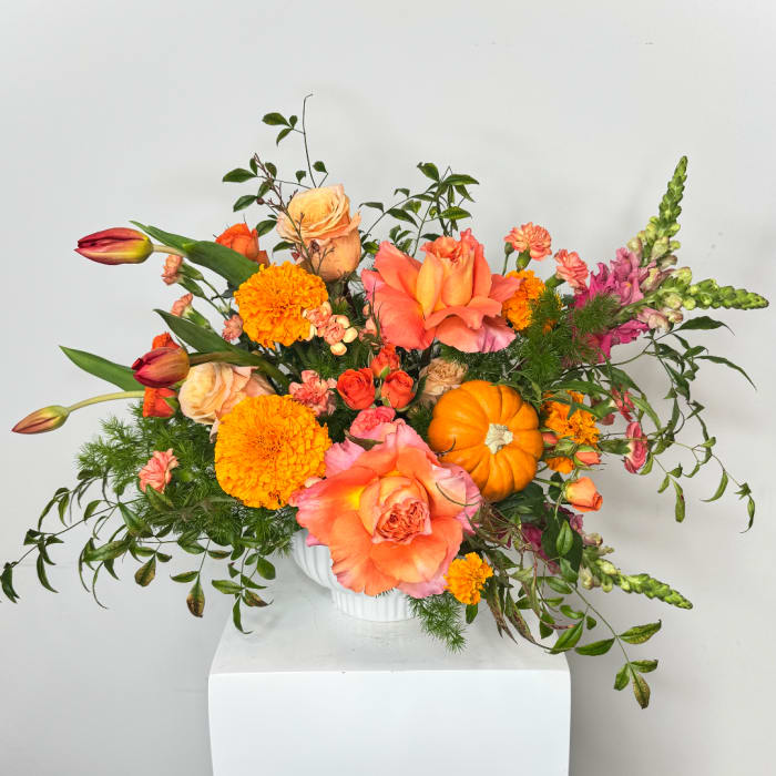 Orange and pink floral arrangement in a white vase with marigolds and roses