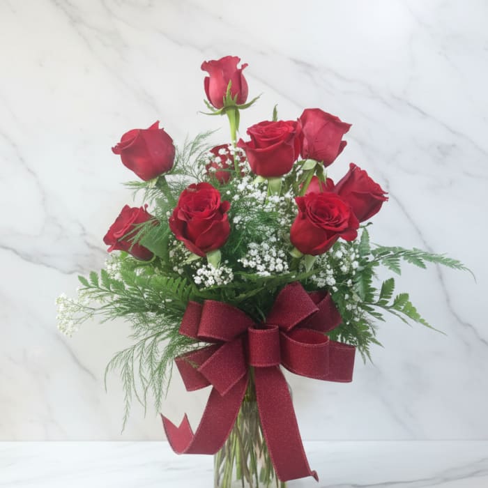 Red roses arranged in a glass vase with a burgundy ribbon