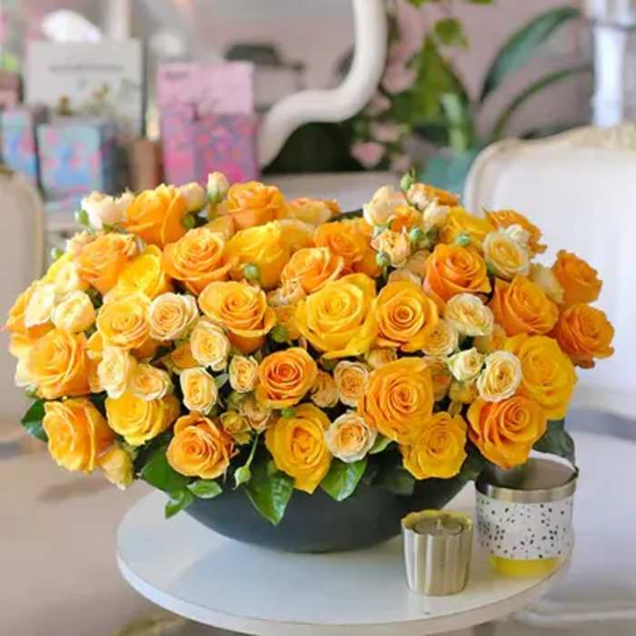 Large bouquet of yellow and orange roses in a dark bowl on a white table