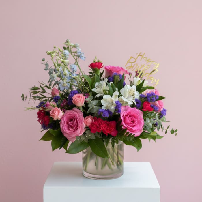 Mixed pink and white flowers in a glass vase with a birthday topper