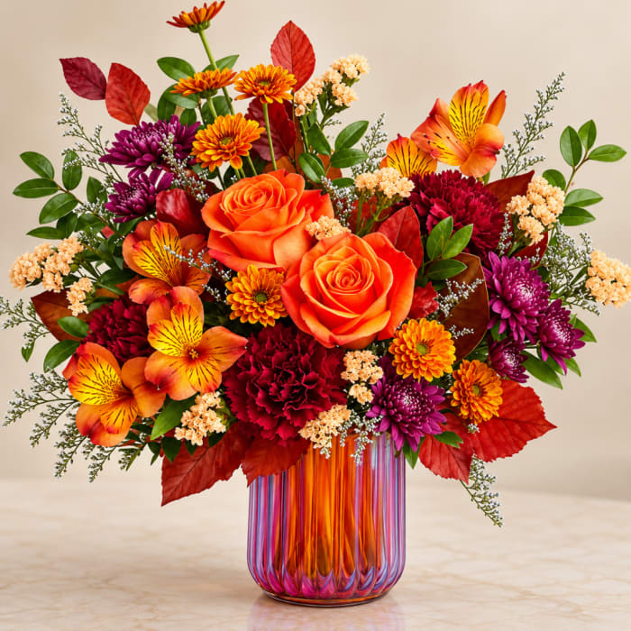 Orange roses and mixed fall flowers in a striped glass vase