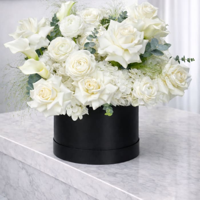 White roses and calla lilies arranged in a black round box