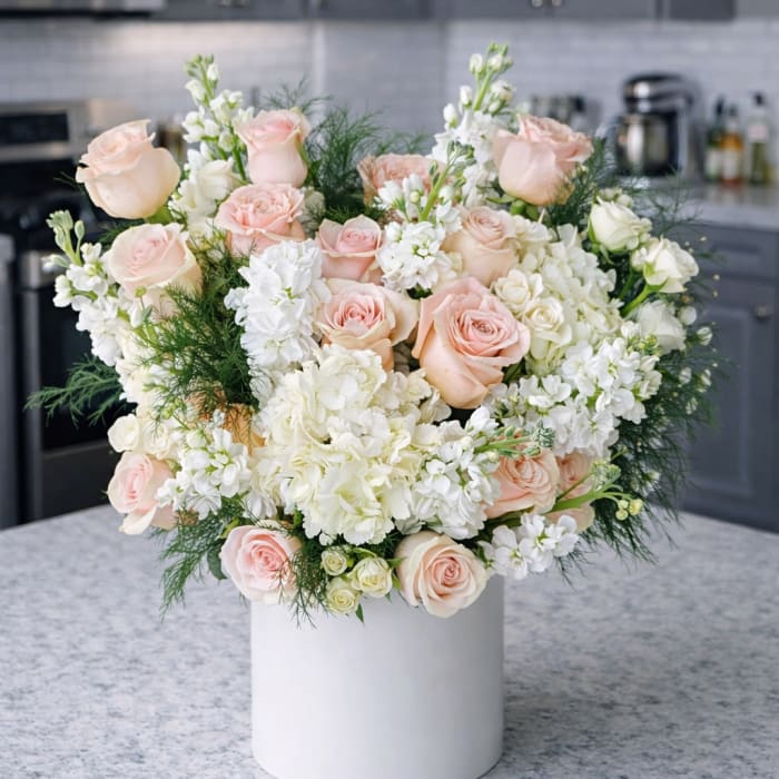 Blush roses and white flowers arranged in a white vase