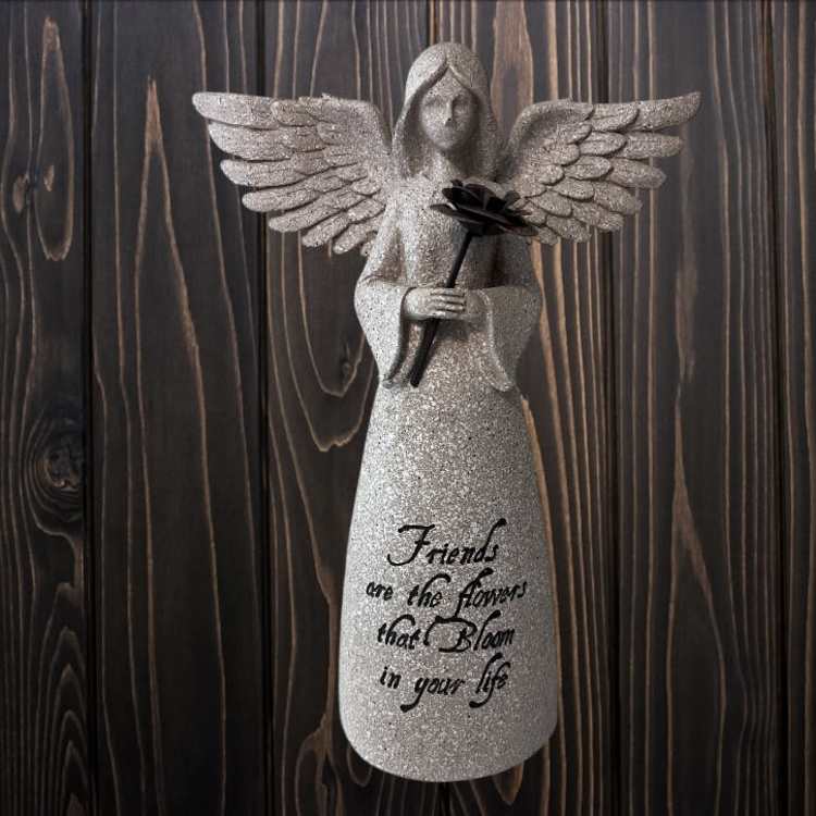 Glittery angel figurine holding a black flower against a wood background