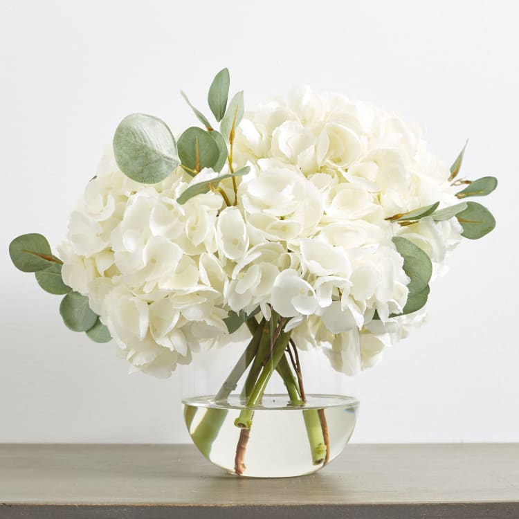 White hydrangea bouquet in a clear glass bowl vase with eucalyptus