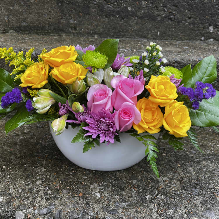 Mixed bouquet of yellow and pink roses in a white bowl vase