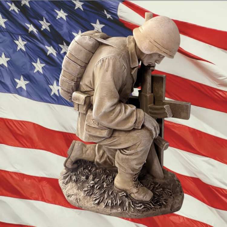 A kneeling soldier statue in front of an American flag.