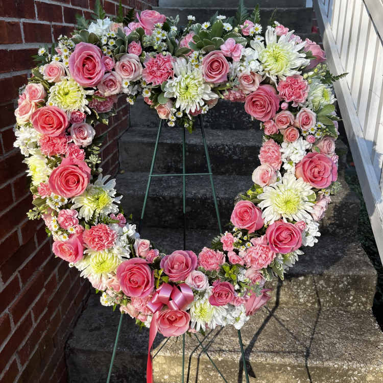 Heart-shaped floral wreath with pink roses and white daisies on a stand