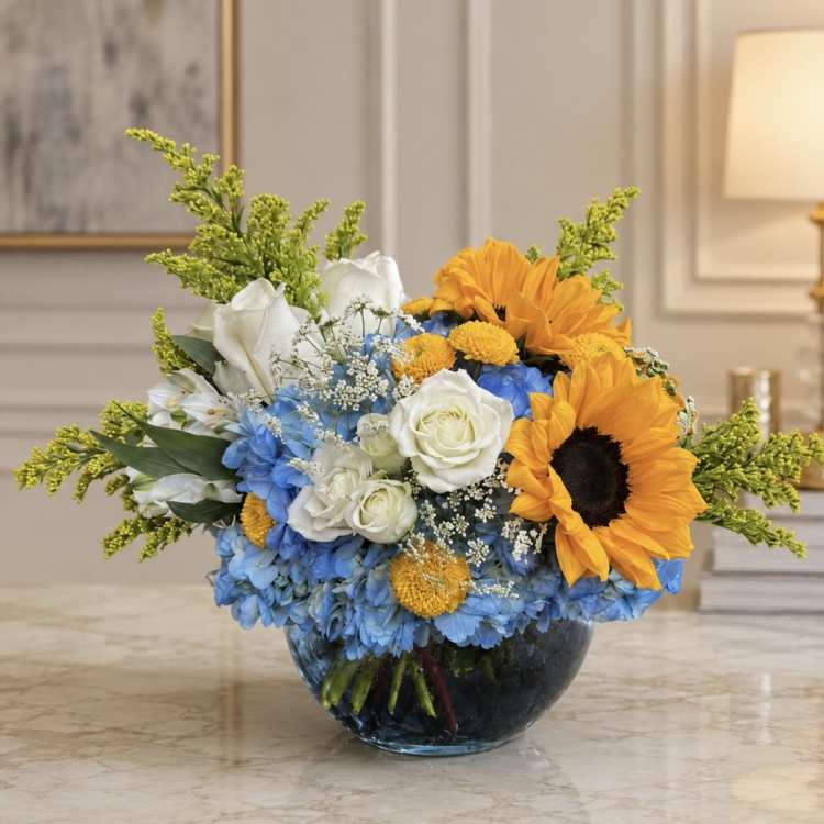 Bouquet of blue hydrangeas, white roses, and orange sunflowers in a glass bowl vase