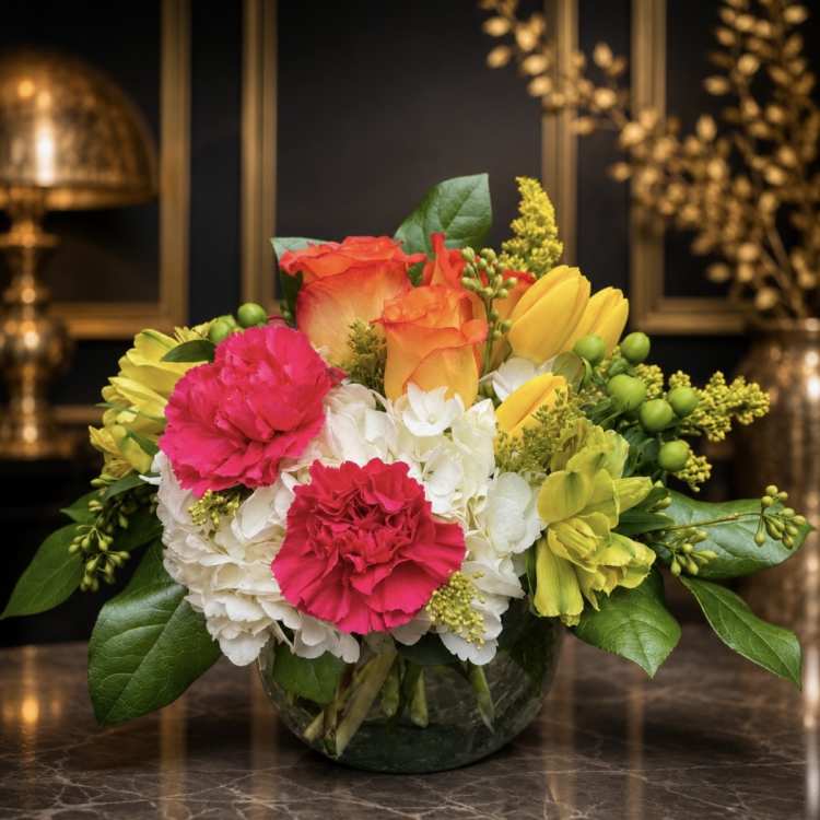 Colorful bouquet of roses, carnations, hydrangeas, and tulips in a glass vase