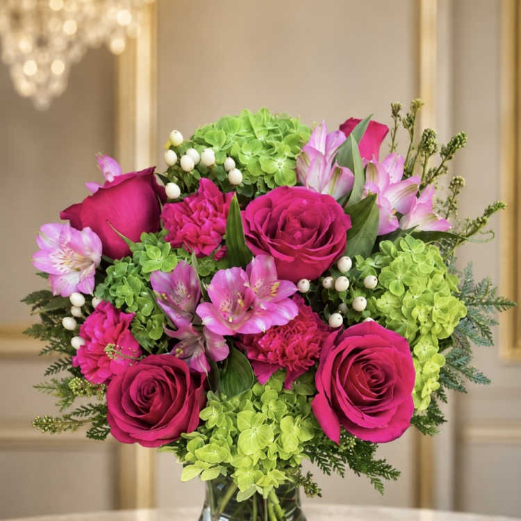 Pink roses and alstroemeria arranged with green hydrangea in a glass vase.