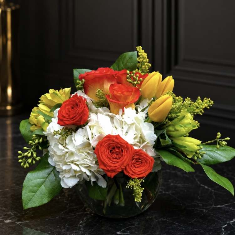 Bouquet of red roses, white hydrangeas, and yellow tulips in a glass vase