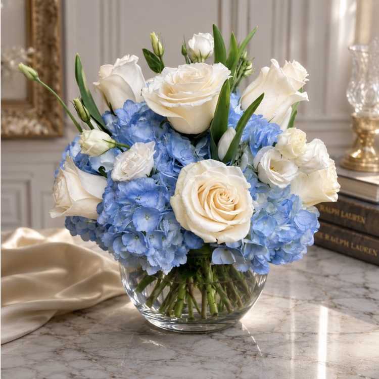 White roses and blue hydrangeas arranged in a clear glass bowl vase