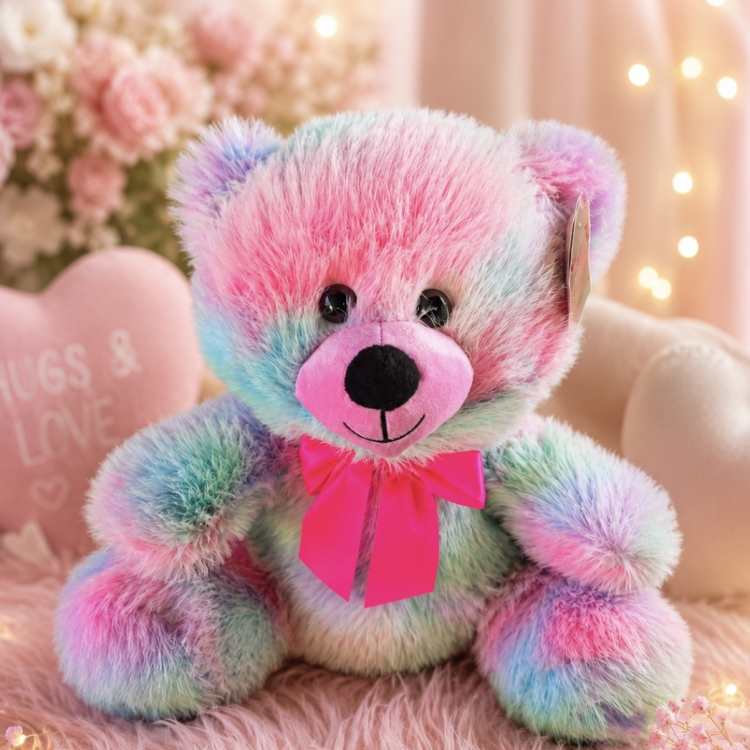 Pastel rainbow teddy bear with a pink bow sitting on a fluffy pink surface