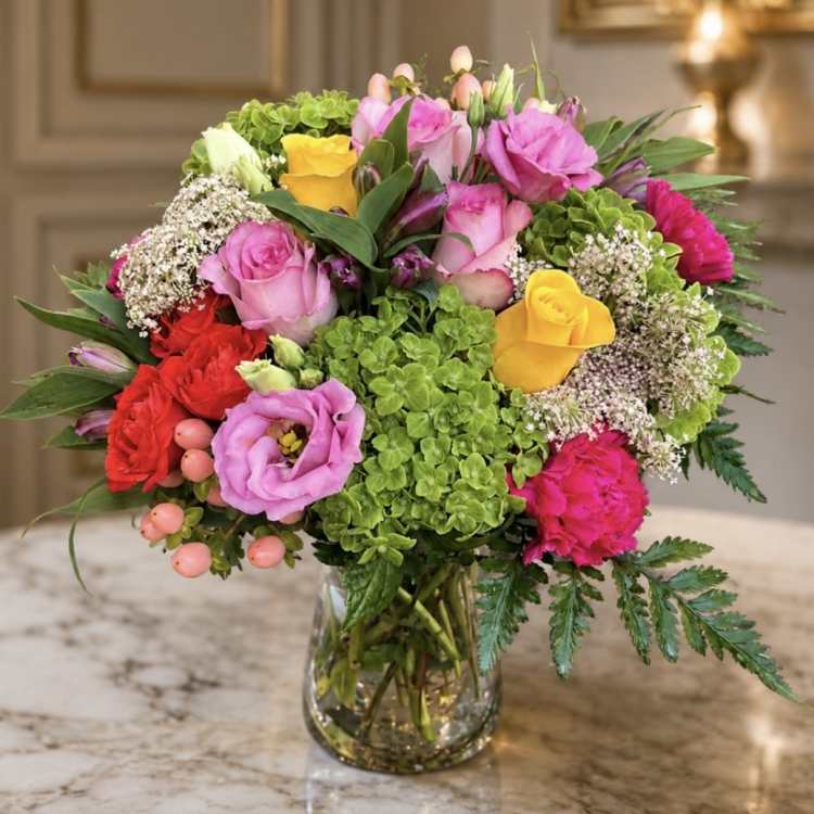 Mixed bouquet of pink, yellow, and red flowers in a glass vase