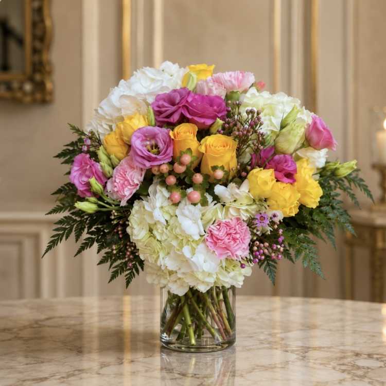 Mixed bouquet of pink, yellow, and white flowers in a clear glass vase