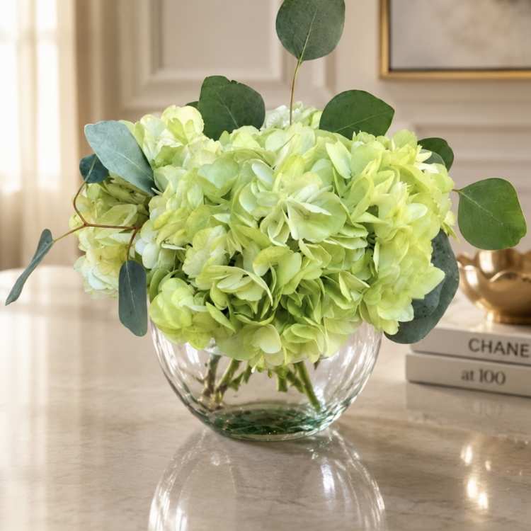 Lime green hydrangeas in a clear glass bowl vase with eucalyptus