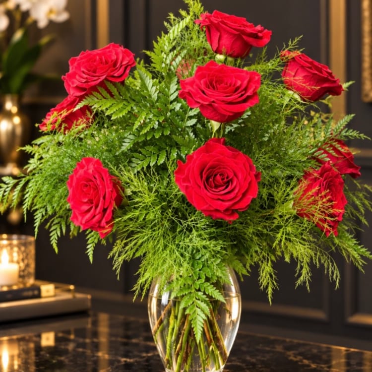 Red roses arranged in a clear glass vase with lush greenery