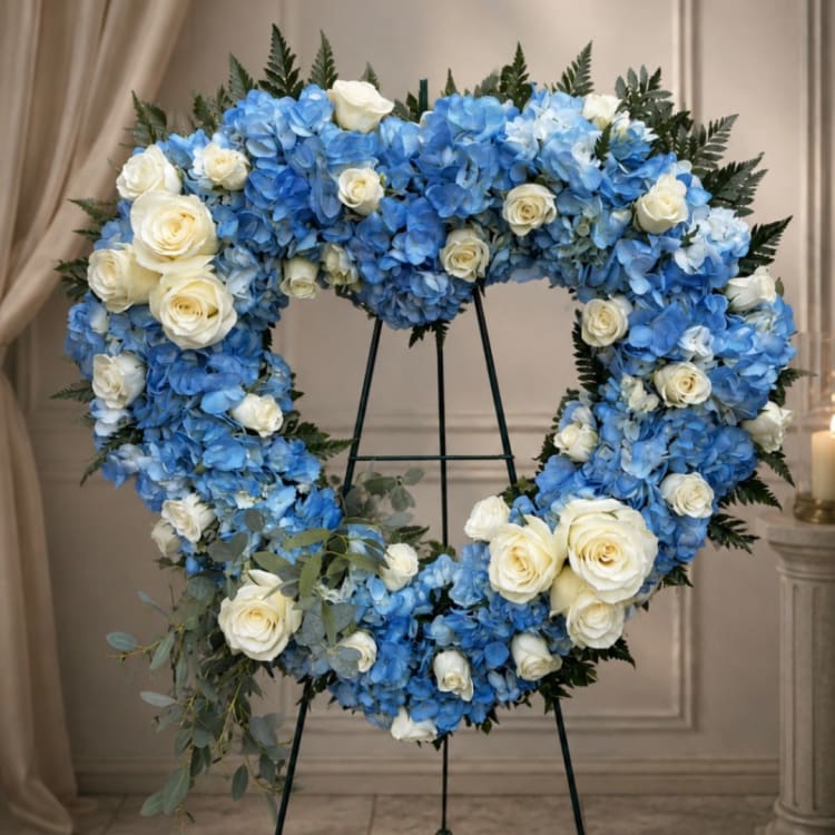 Heart-shaped floral wreath of blue hydrangeas and white roses on a stand