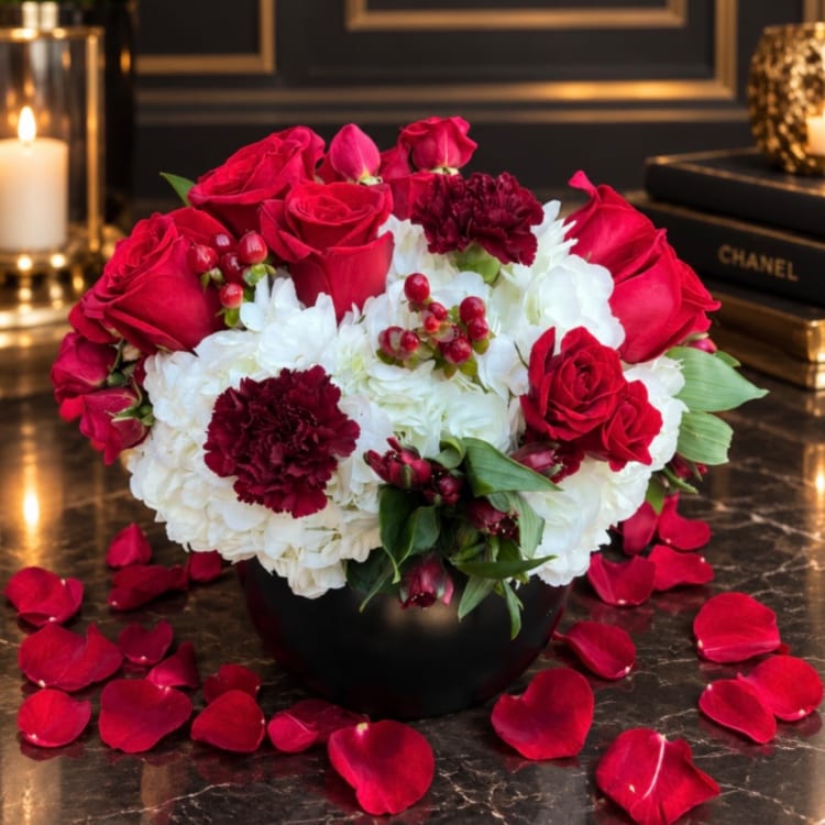 Red roses and white hydrangeas arranged in a black vase with scattered rose petals