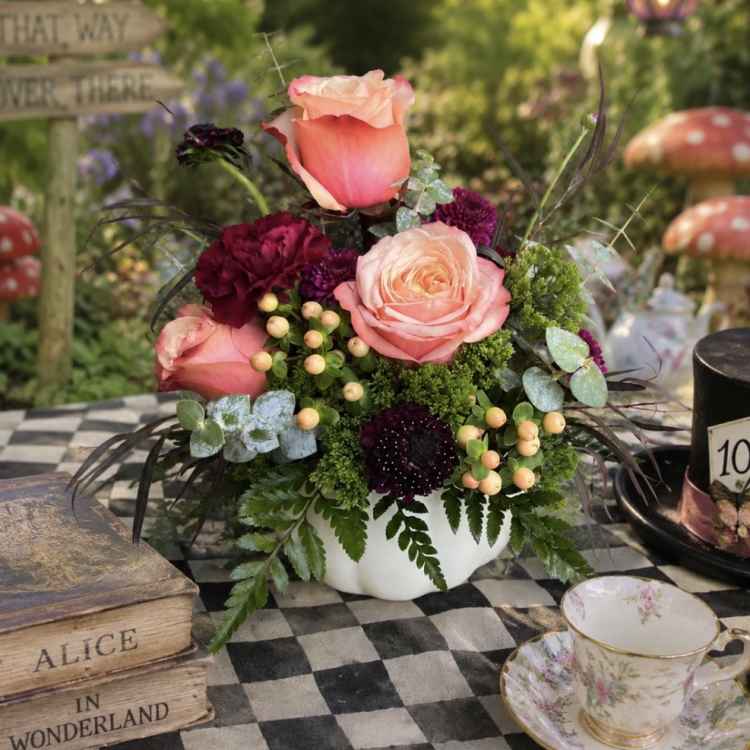 Pink and peach roses arranged in a white bowl with dark burgundy blooms