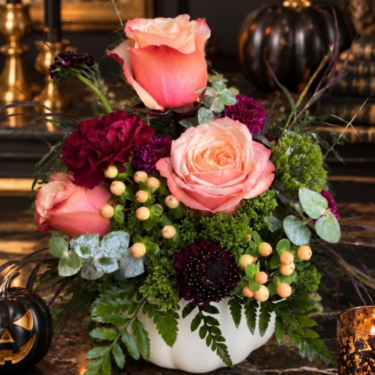 Pink and peach roses arranged in a white vase with dark purple flowers
