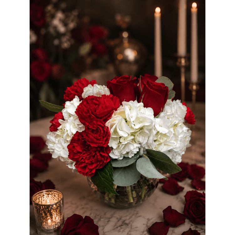 Red roses and white carnations in a glass vase with candles