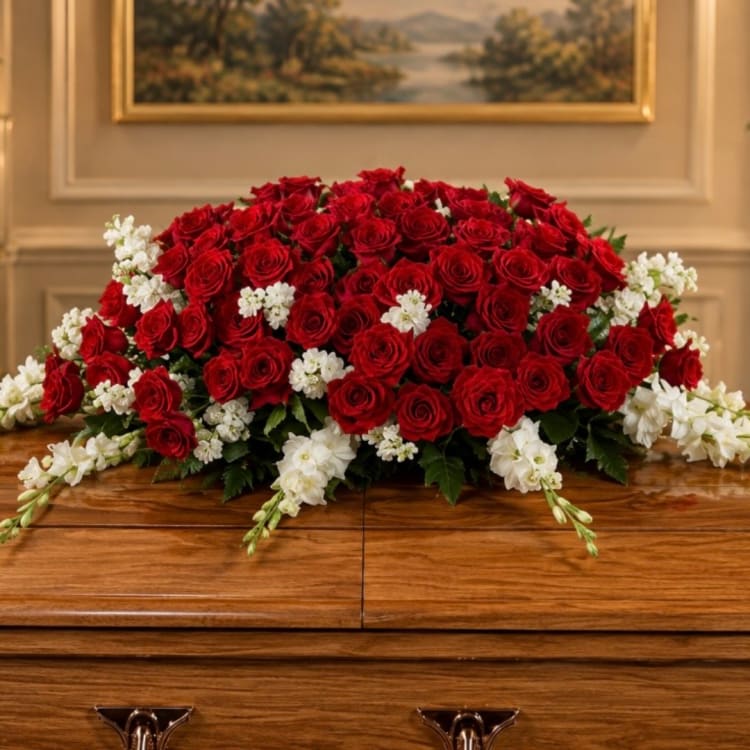 Large red rose arrangement with white accent flowers on a wooden casket