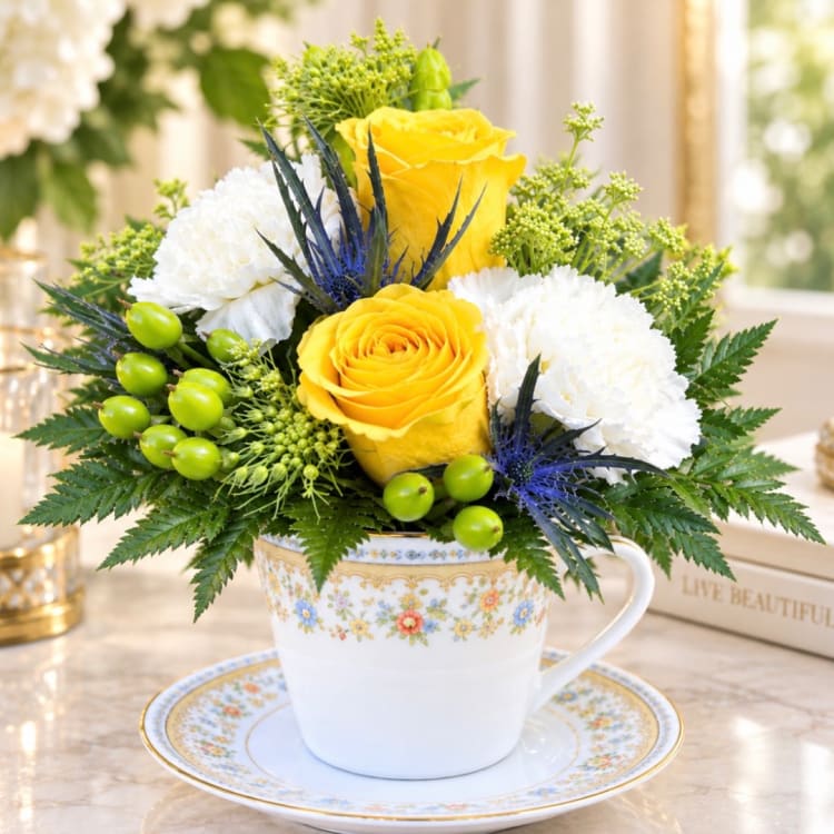 Yellow and white flower arrangement in a floral teacup and saucer