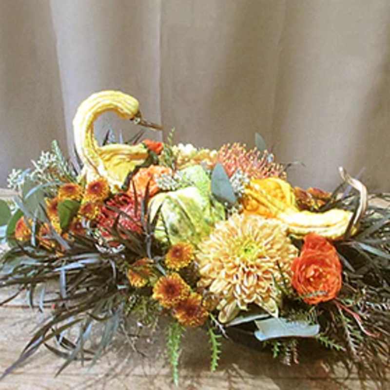Low autumn centerpiece with gourd swans and orange and yellow flowers in an oval arrangement