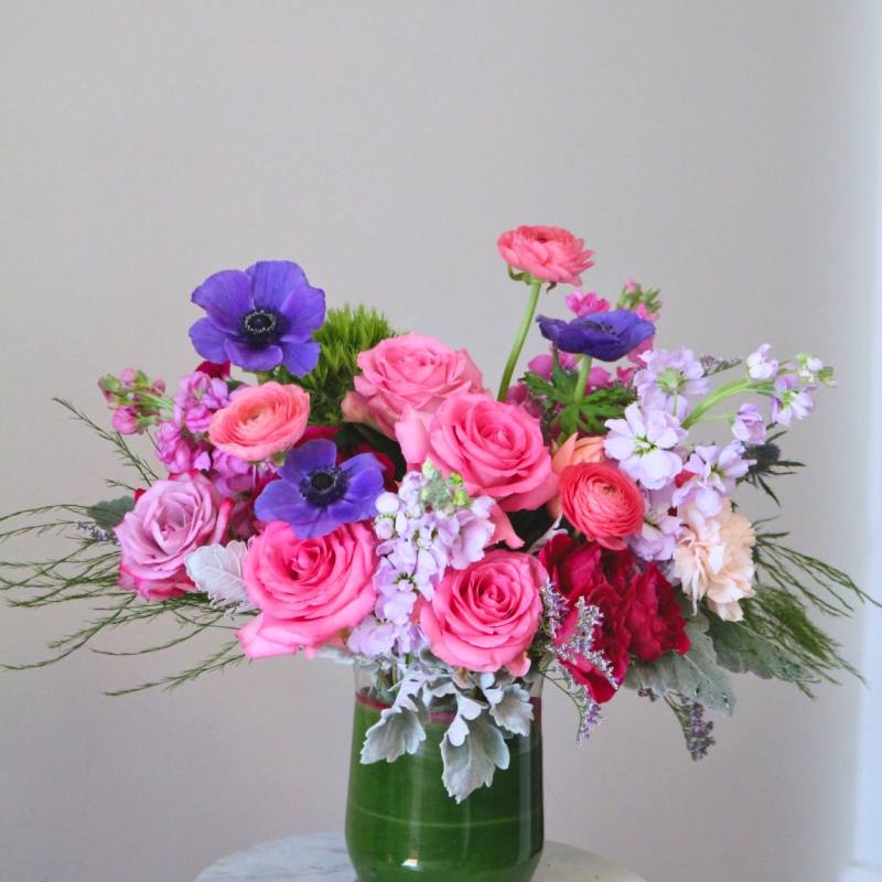 Pink and purple mixed flower arrangement in a green glass vase