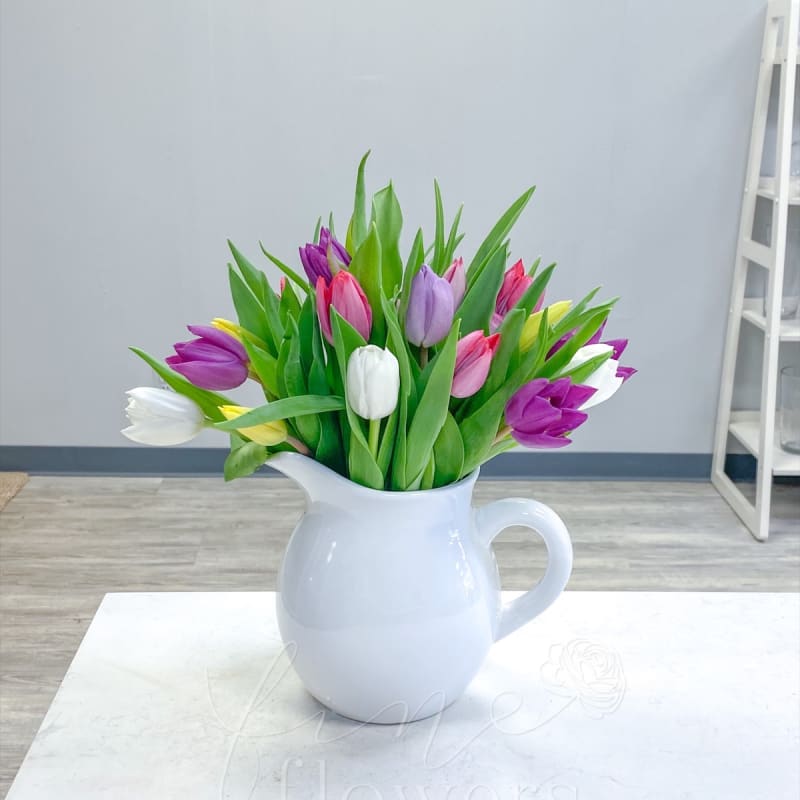Mixed tulip arrangement in a white ceramic pitcher on a light table